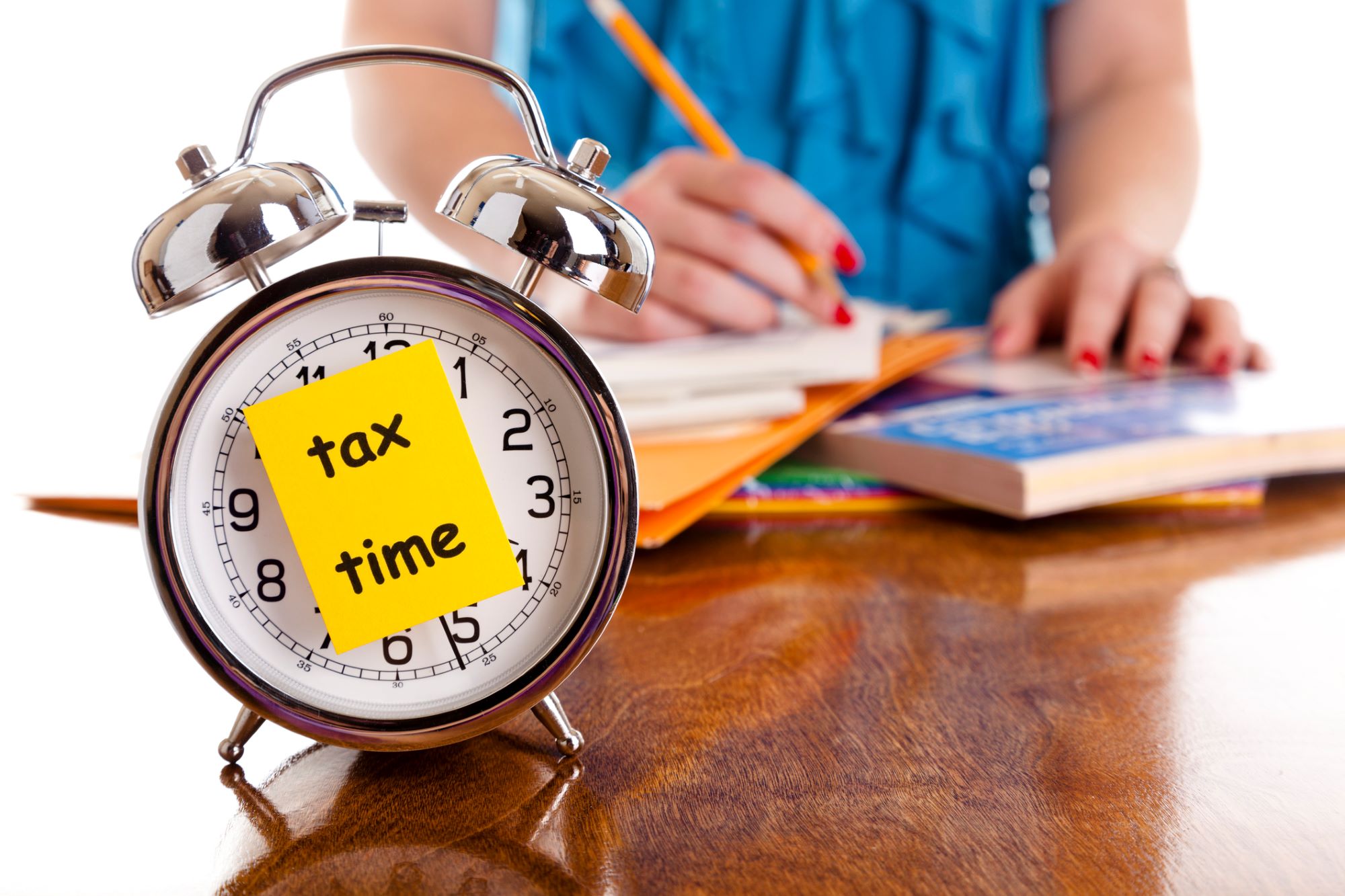 Clock with tax time sticky note and woman doing her taxes.